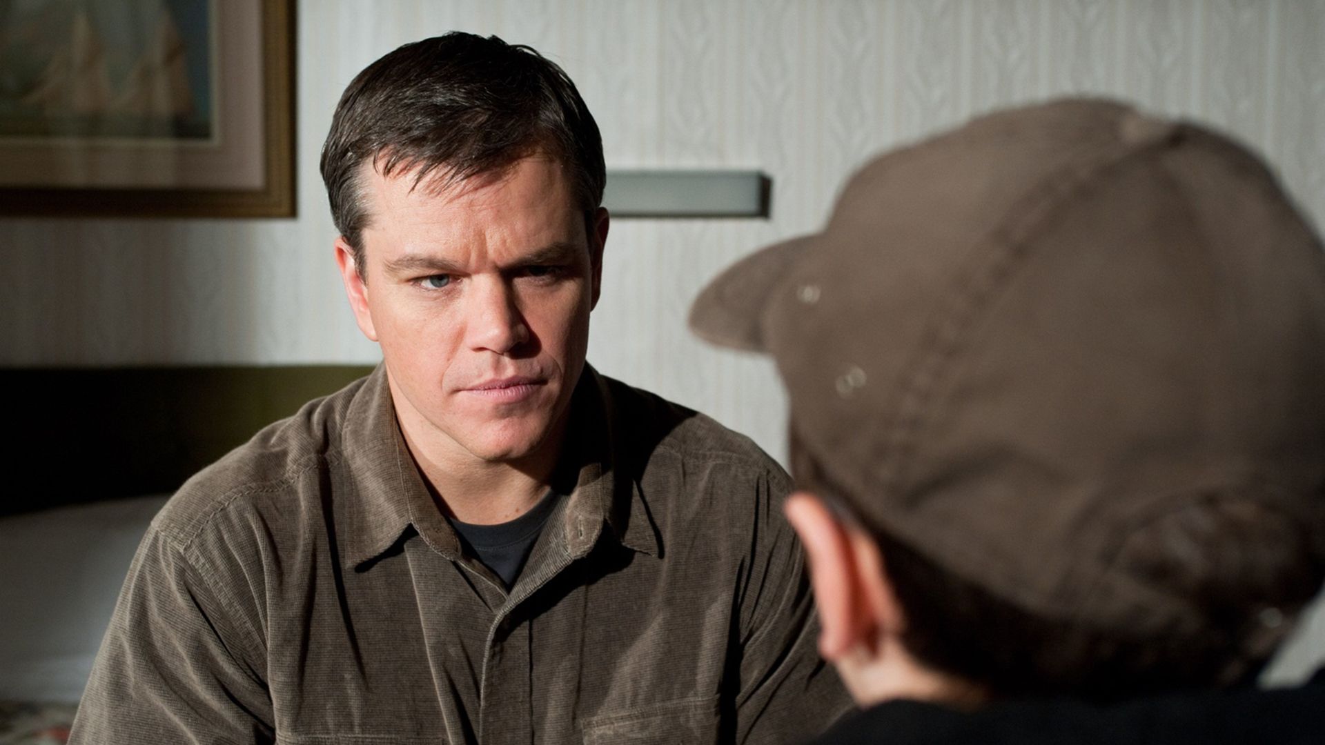 A man in a brown corduroy shirt sits in front of a boy in a brown baseball cap