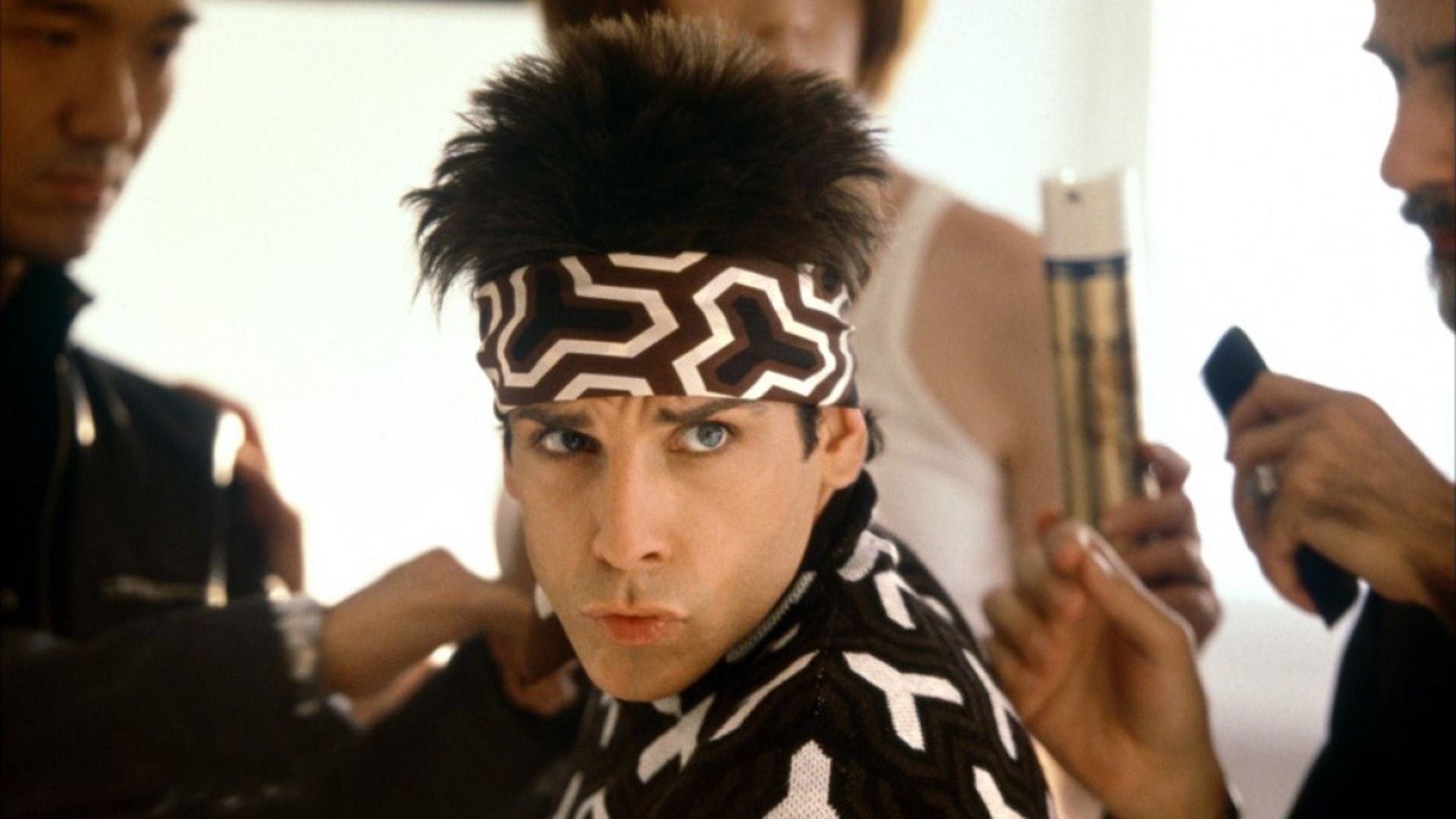 A fashionably dressed man with a headband surrounded by hairdressers