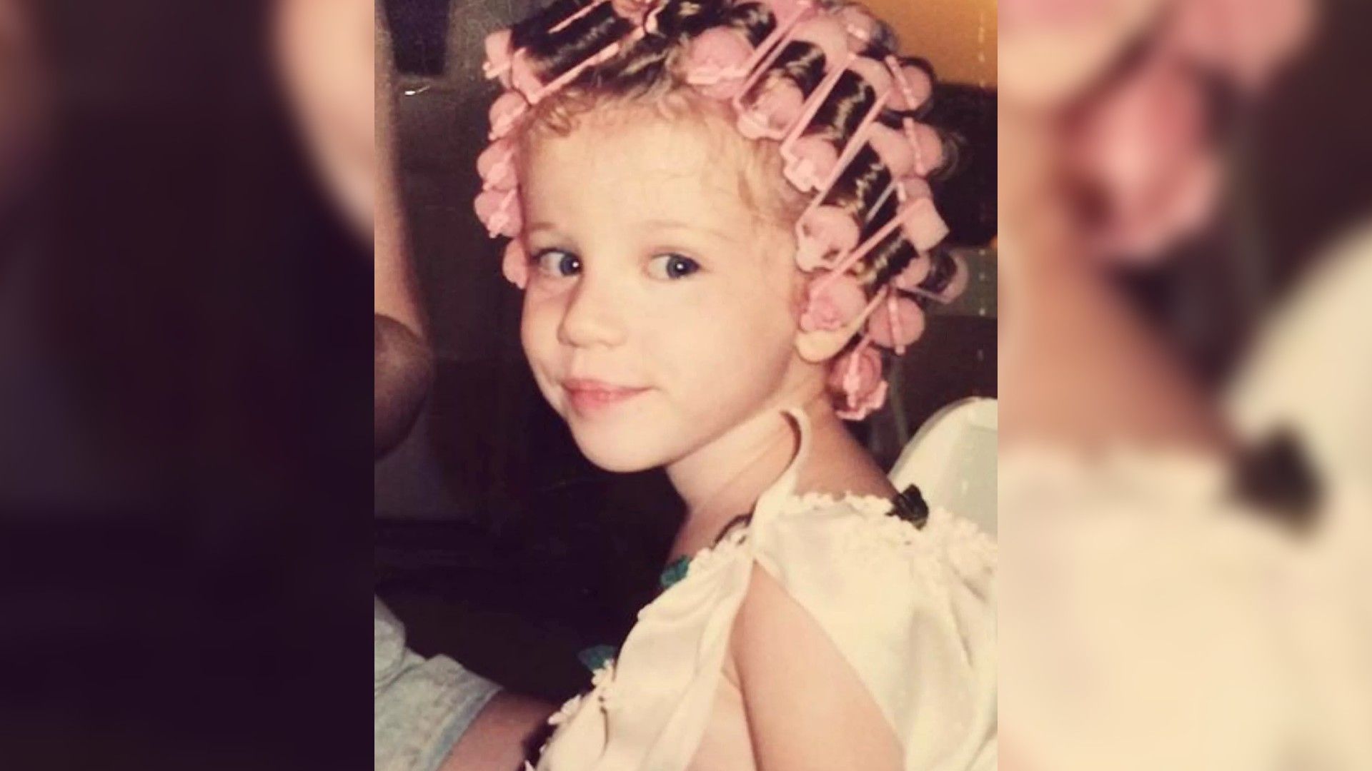 A little girl in a white dress with pink curlers in her hair