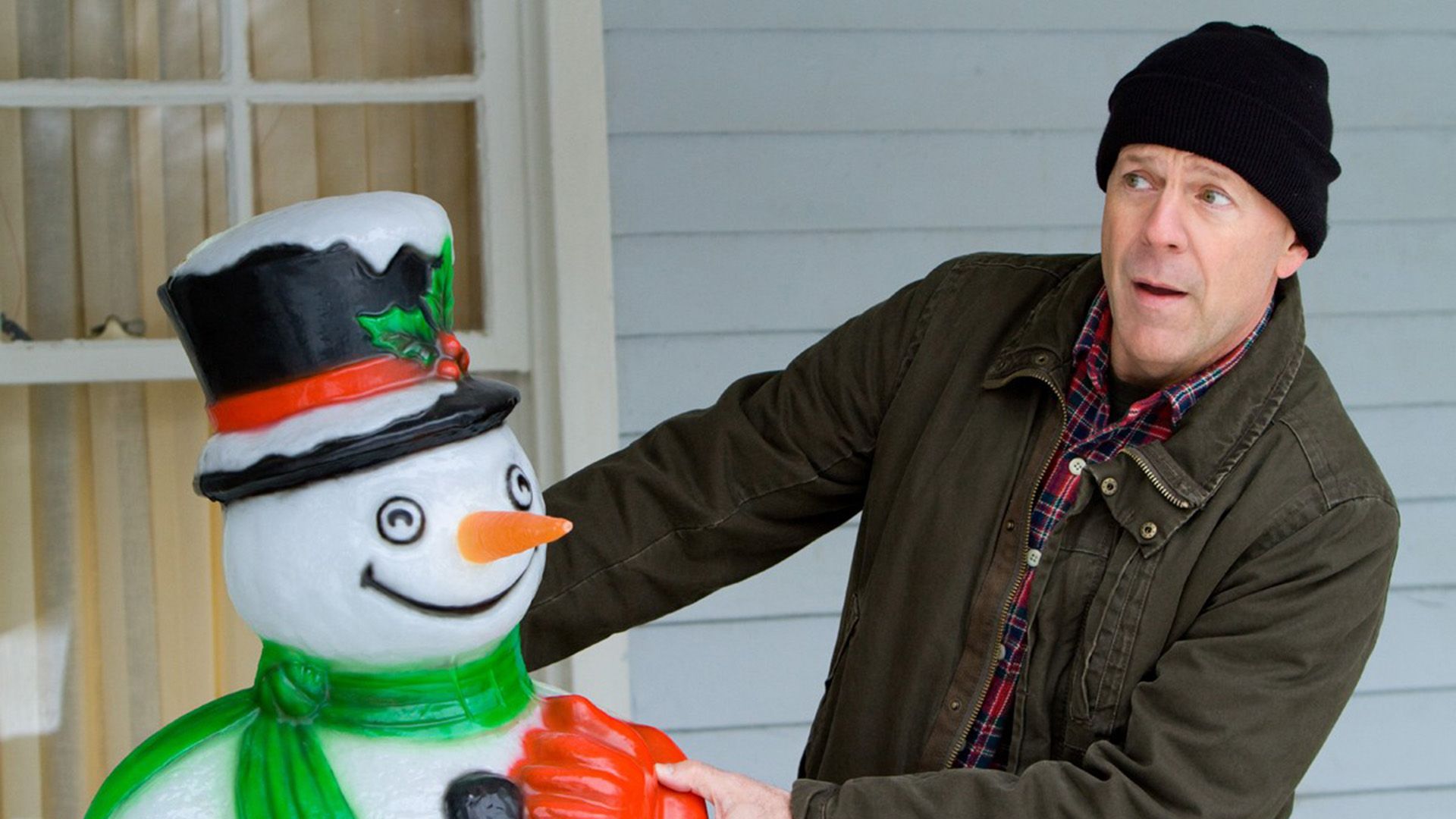 A man in a black hat is peeking out from behind a snowman figure