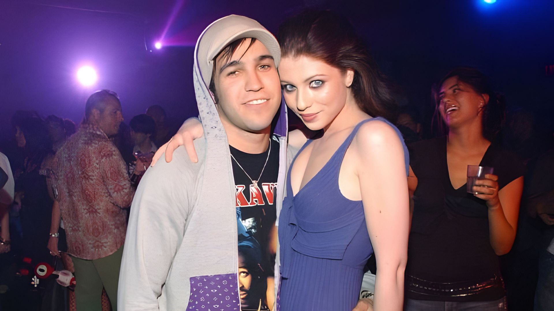 Actress Michelle Trachtenberg and musician Pete Wentz are hugging while people are having fun in the background