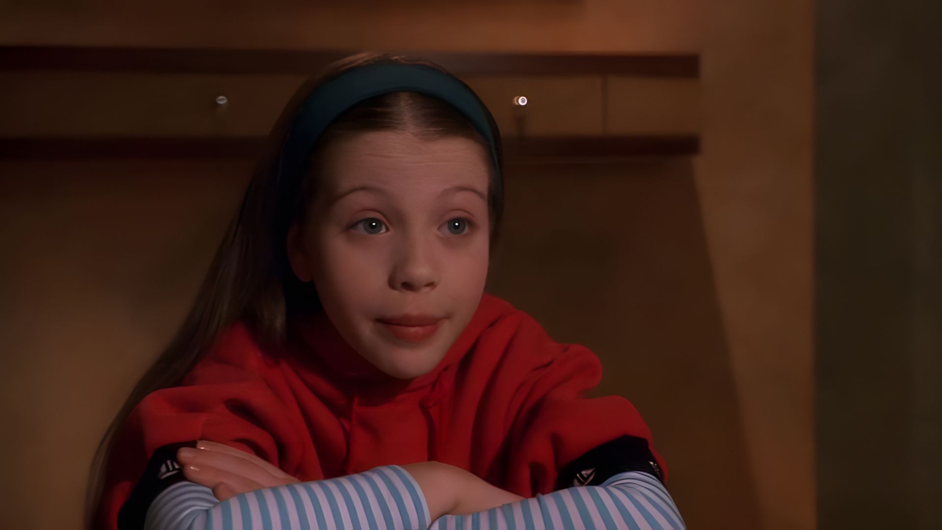 Actress Michelle Trachtenberg as a child, wearing a red sweater, striped arm warmers, and a green headband