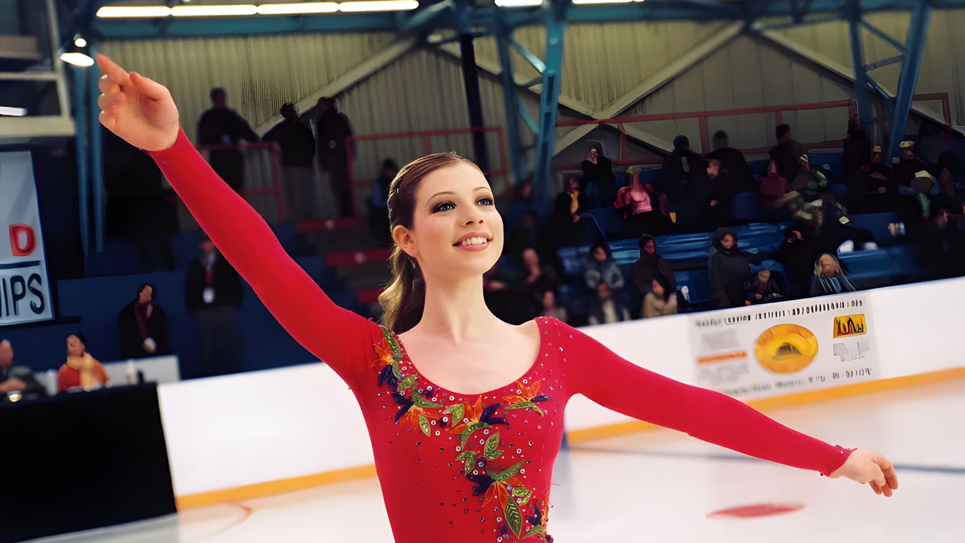 Michelle Trachtenberg in a red skater costume dances on the ice, arms raised upwards