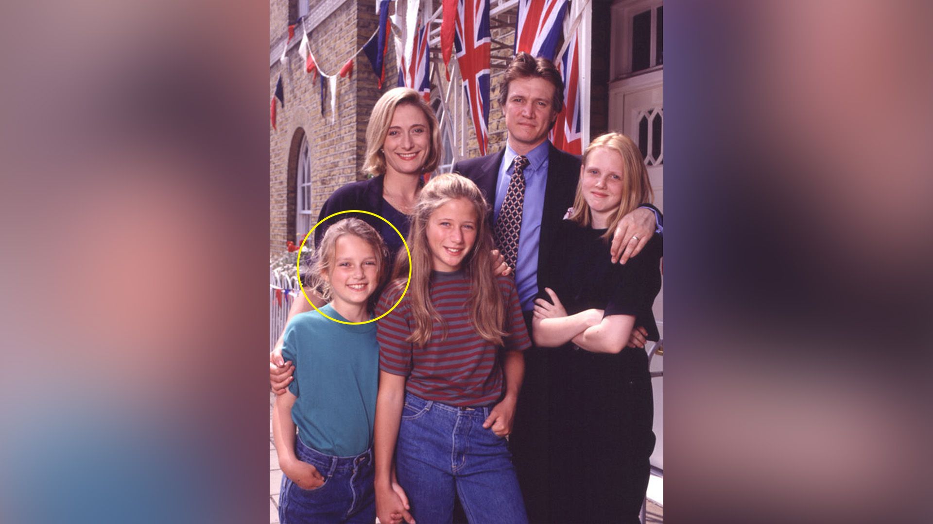 A family with three children stands against the backdrop of a brick building with flags of the United Kingdom