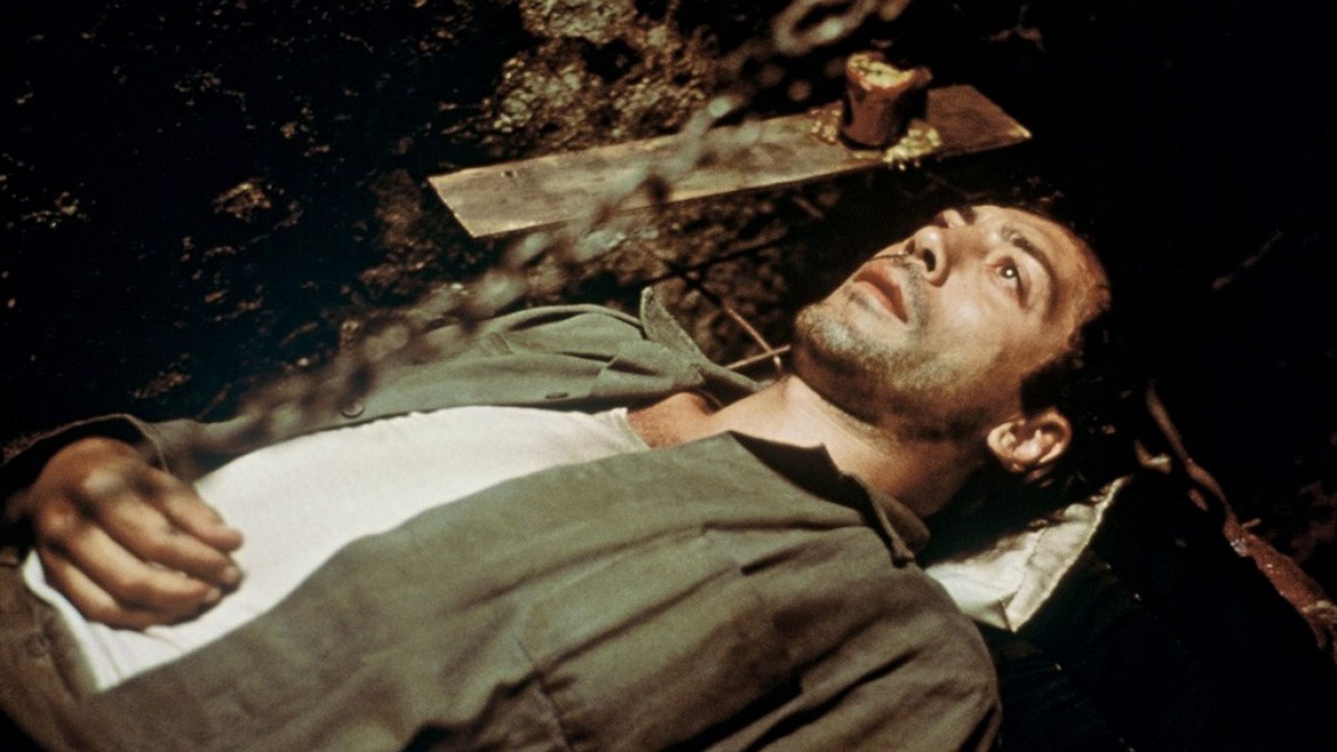 A man in a green shirt and white tank top is lying on his back and looking at the ceiling