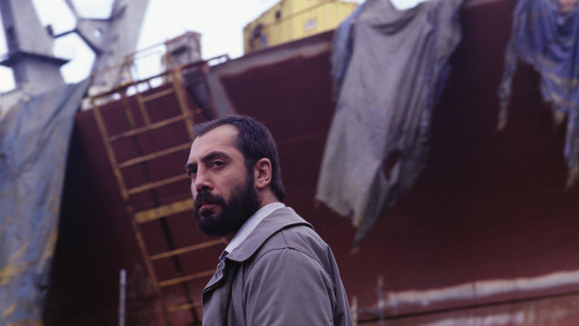 A man with a beard and mustache against the background of a reddish-brown ship