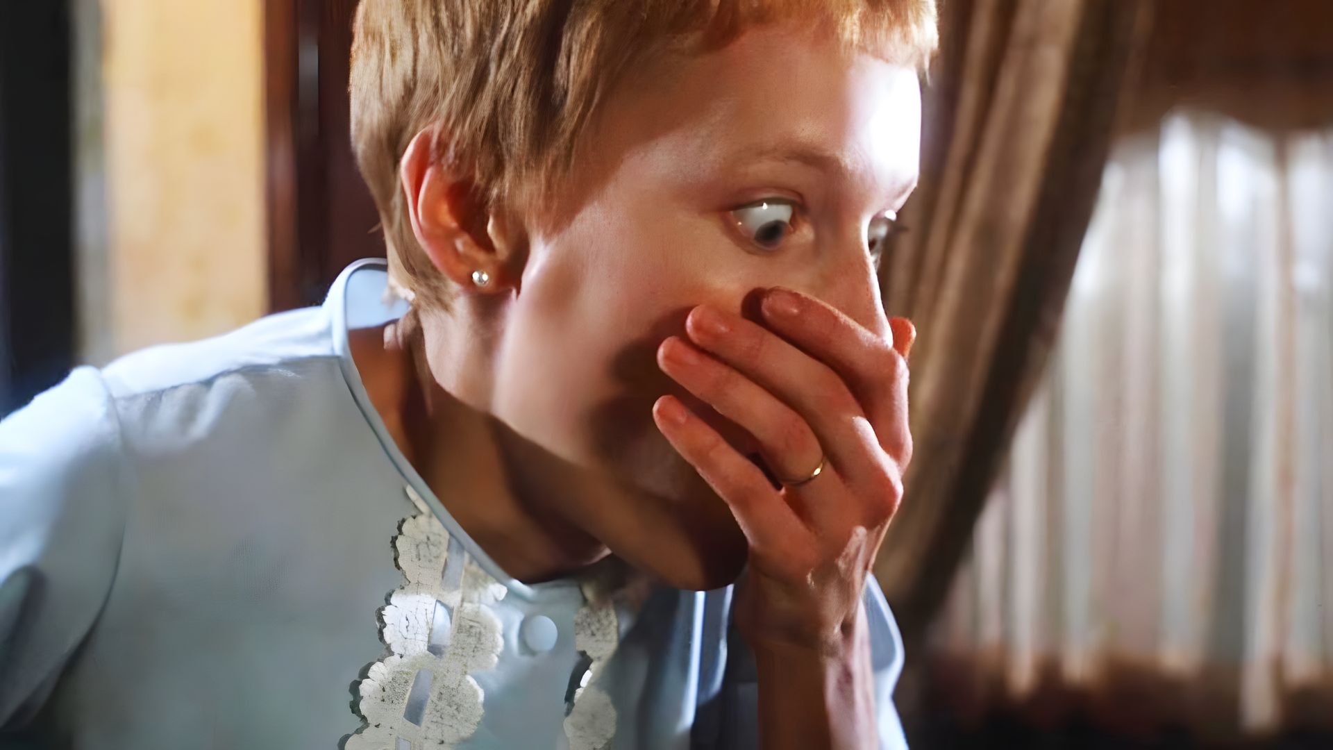 Actress Mia Farrow with a short haircut covers her mouth with her hand in fear