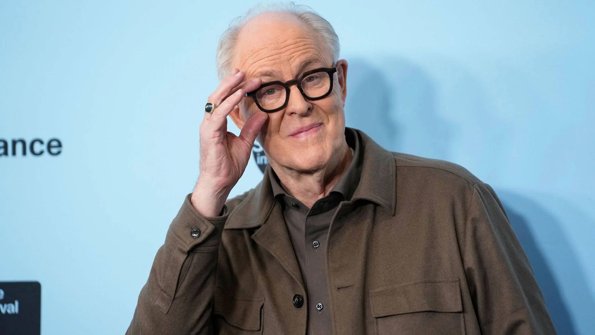 Actor John Lithgow adjusts his glasses in a black frame