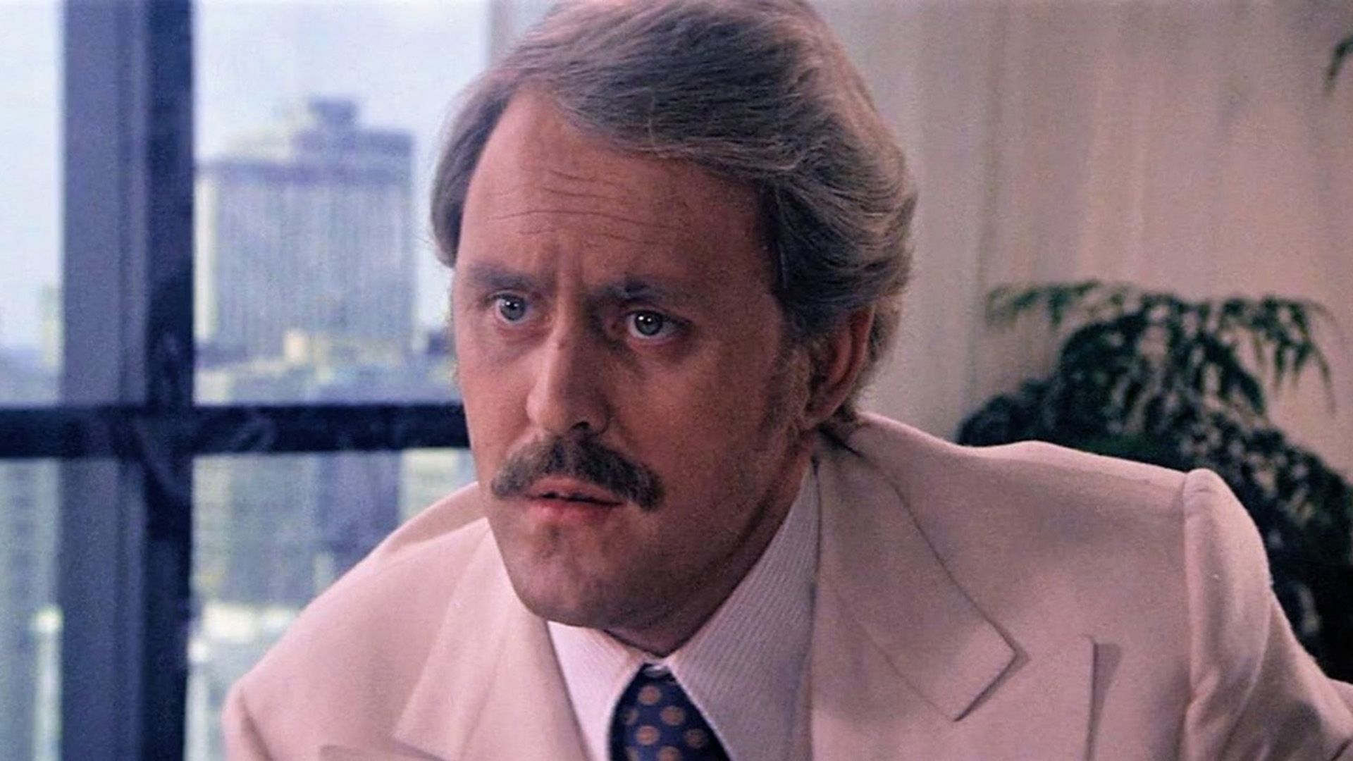 John Lithgow with a mustache and in a cream jacket in a frame from the film "Obsession"
