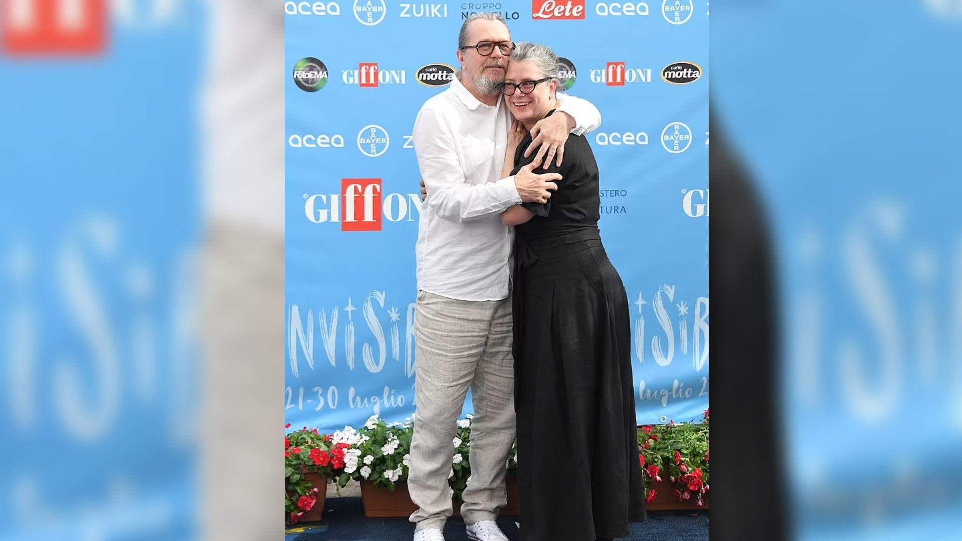 Gary Oldman and Gisele Schmidt hugging and smiling against a blue banner with Giffoni logos