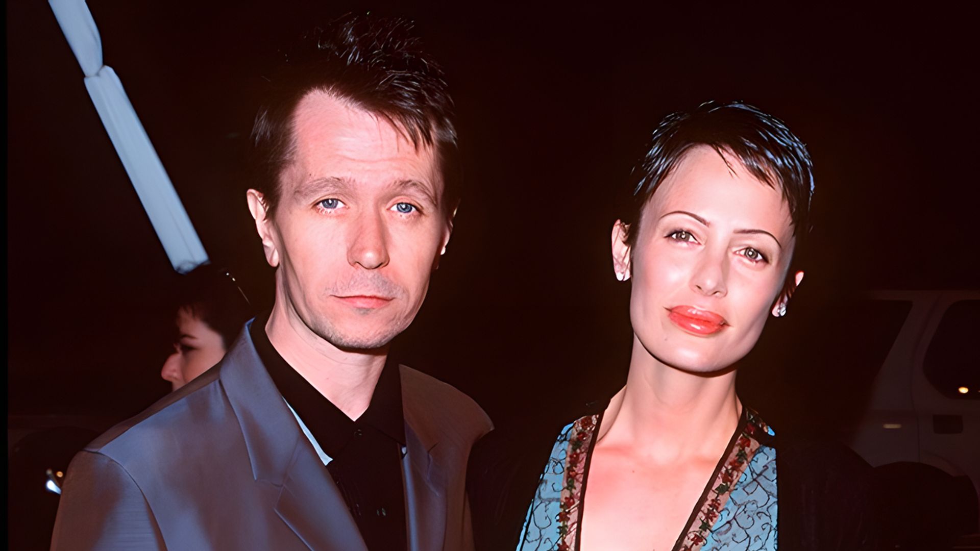 Gary Oldman in a dark suit and Donya Fiorentino in an elegant dress pose together at an evening event.