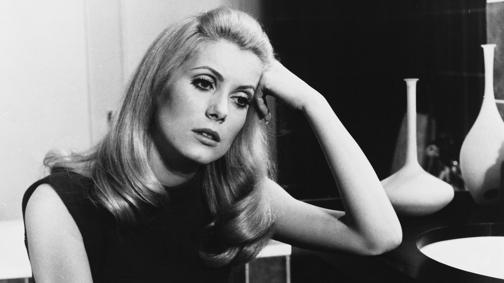 Catherine Deneuve thoughtfully leans on the table in a scene from the film 'Belle de Jour'