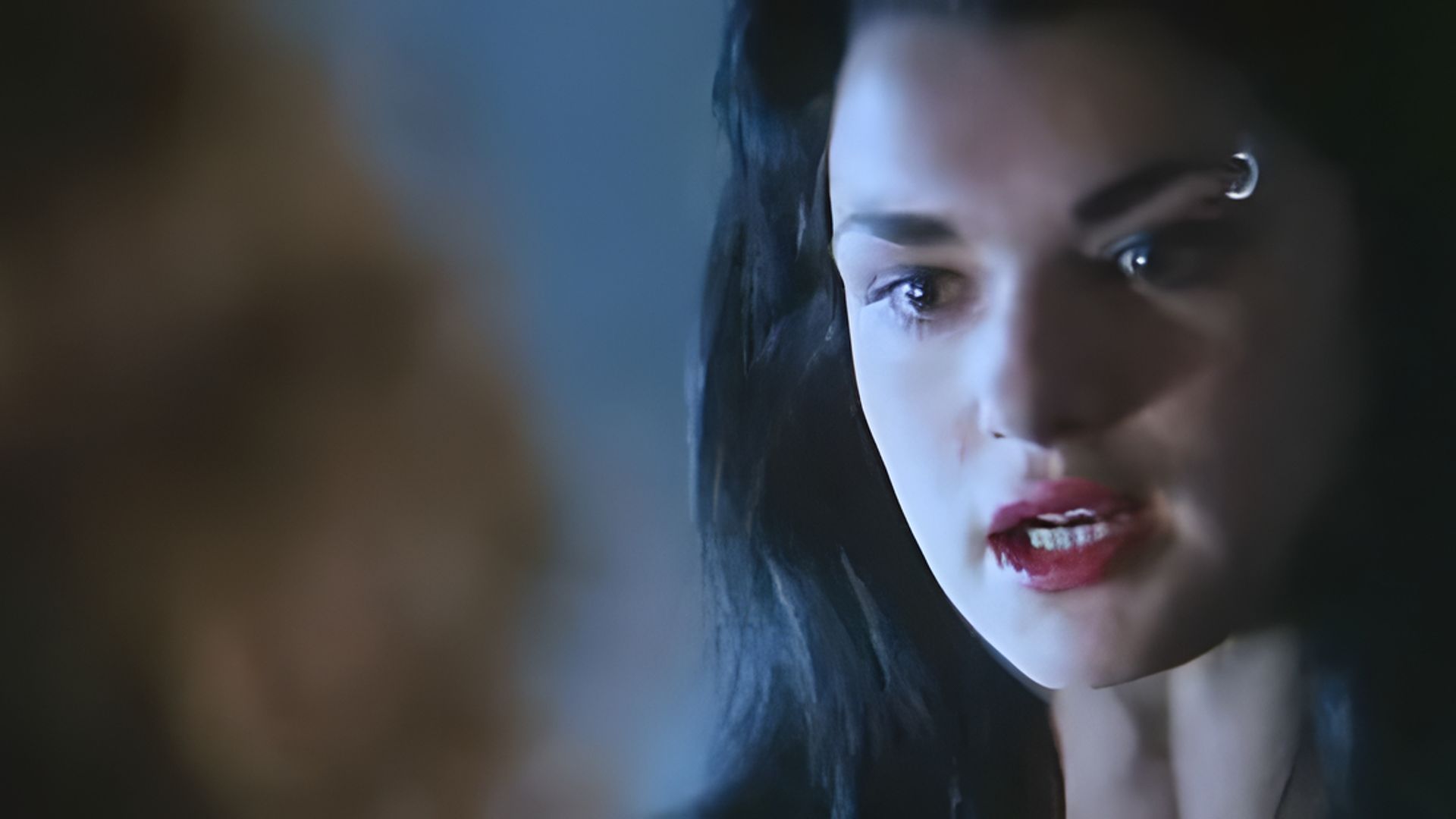 A close-up of Rachel Weisz's face, she has bright red lipstick and a ring in her eyebrow