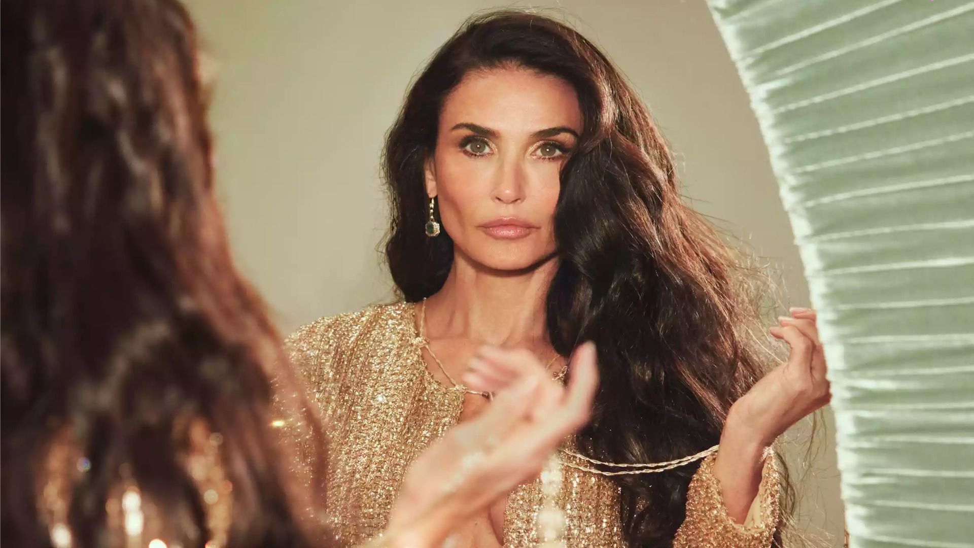 Actress Demi Moore stands in front of a mirror in a golden dress and looks at herself in the reflection