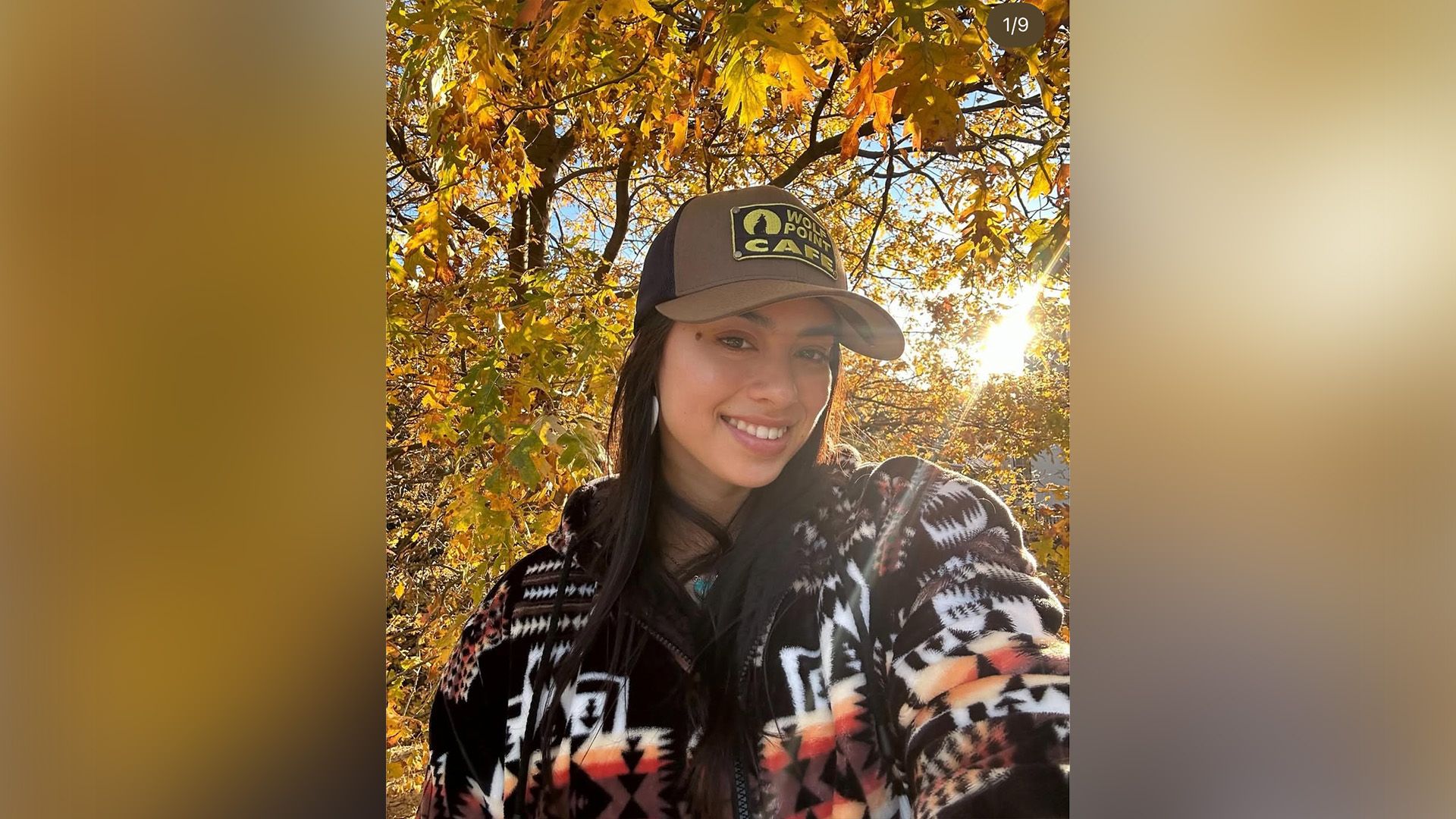 Actress Amber Midthunder in a baseball cap and warm sweater against a backdrop of autumn foliage