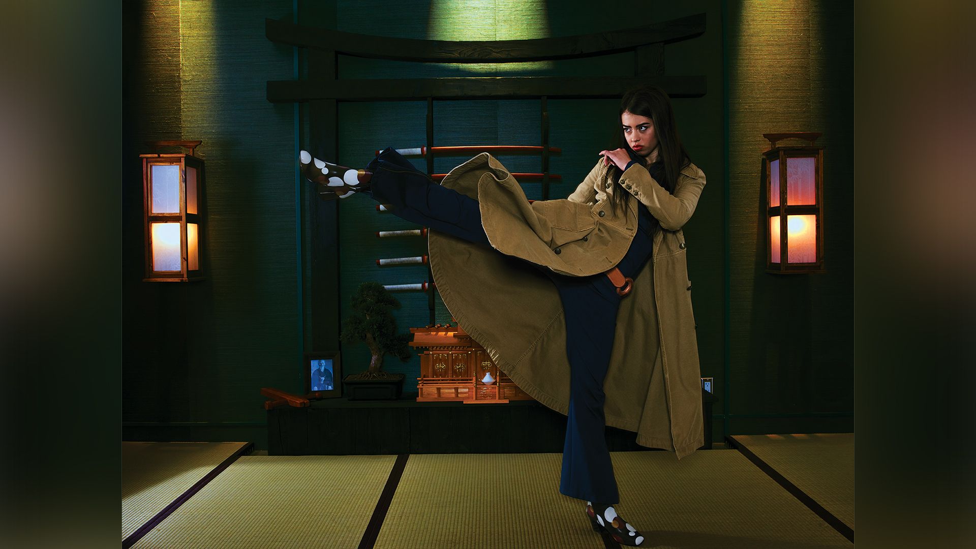 Actress Amber Midthunder in a beige coat with her leg raised in a kick