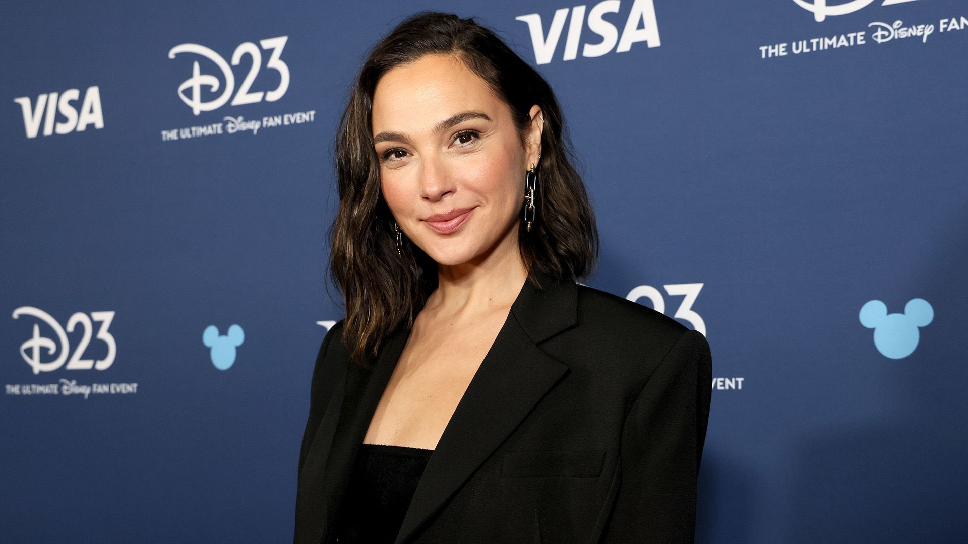 Actress Gal Gadot in a black jacket against a blue background