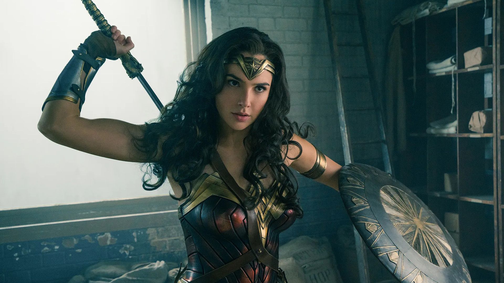 Gal Gadot as Wonder Woman: in armor, holding a shield with her left hand, drawing a sword from behind her back with her right hand