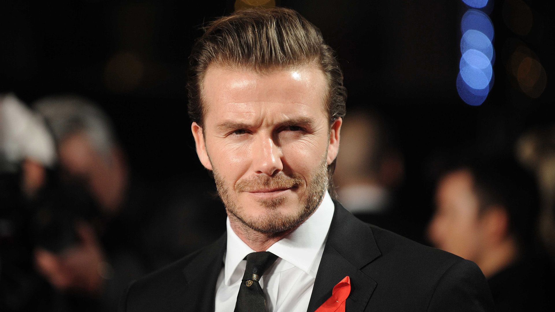 Footballer David Beckham in a black jacket with a red ribbon pinned to it