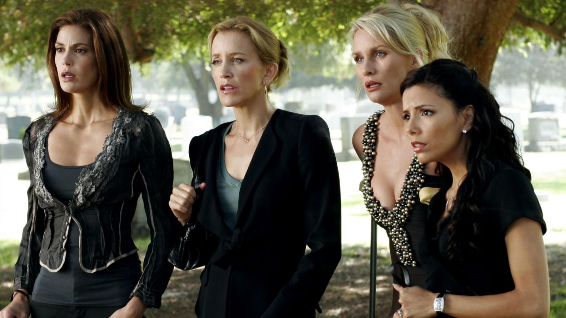 Four women in black clothing look surprised to the side against the backdrop of trees