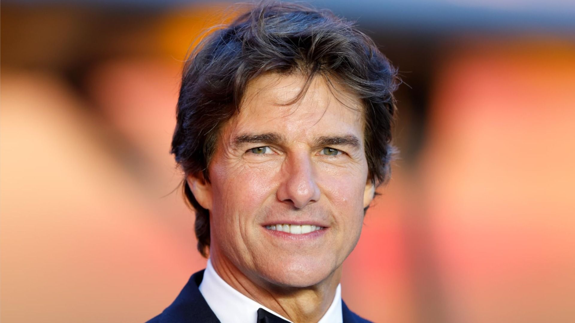 Actor Tom Cruise poses in a classic suit and smiles at the camera against a blurred background
