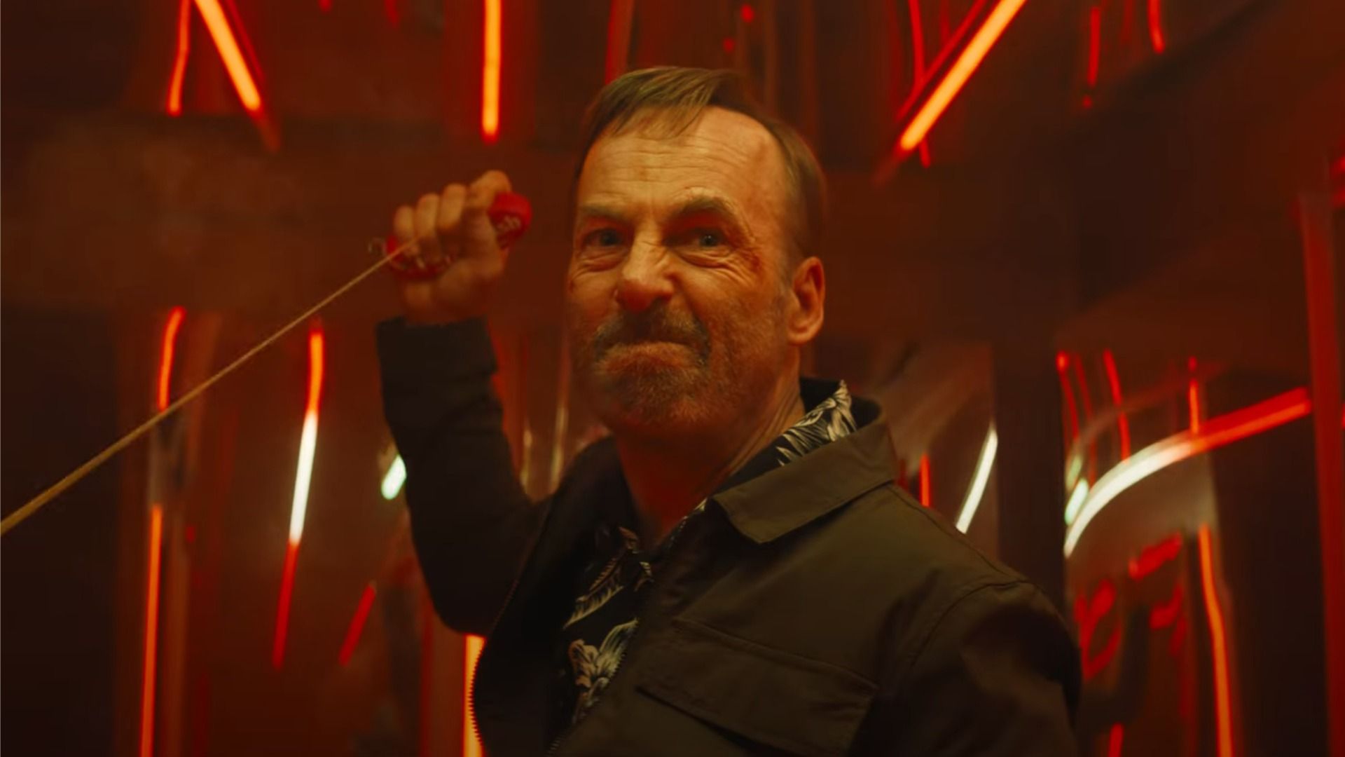 Actor Bob Odenkirk in a black jacket holds a rope in his hands and looks angrily in the direction of the red light