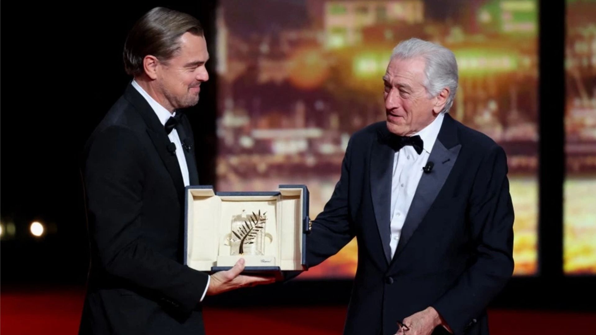 Actor Leonardo DiCaprio smiles as he hands Robert De Niro the 'Palme d'Or' on stage