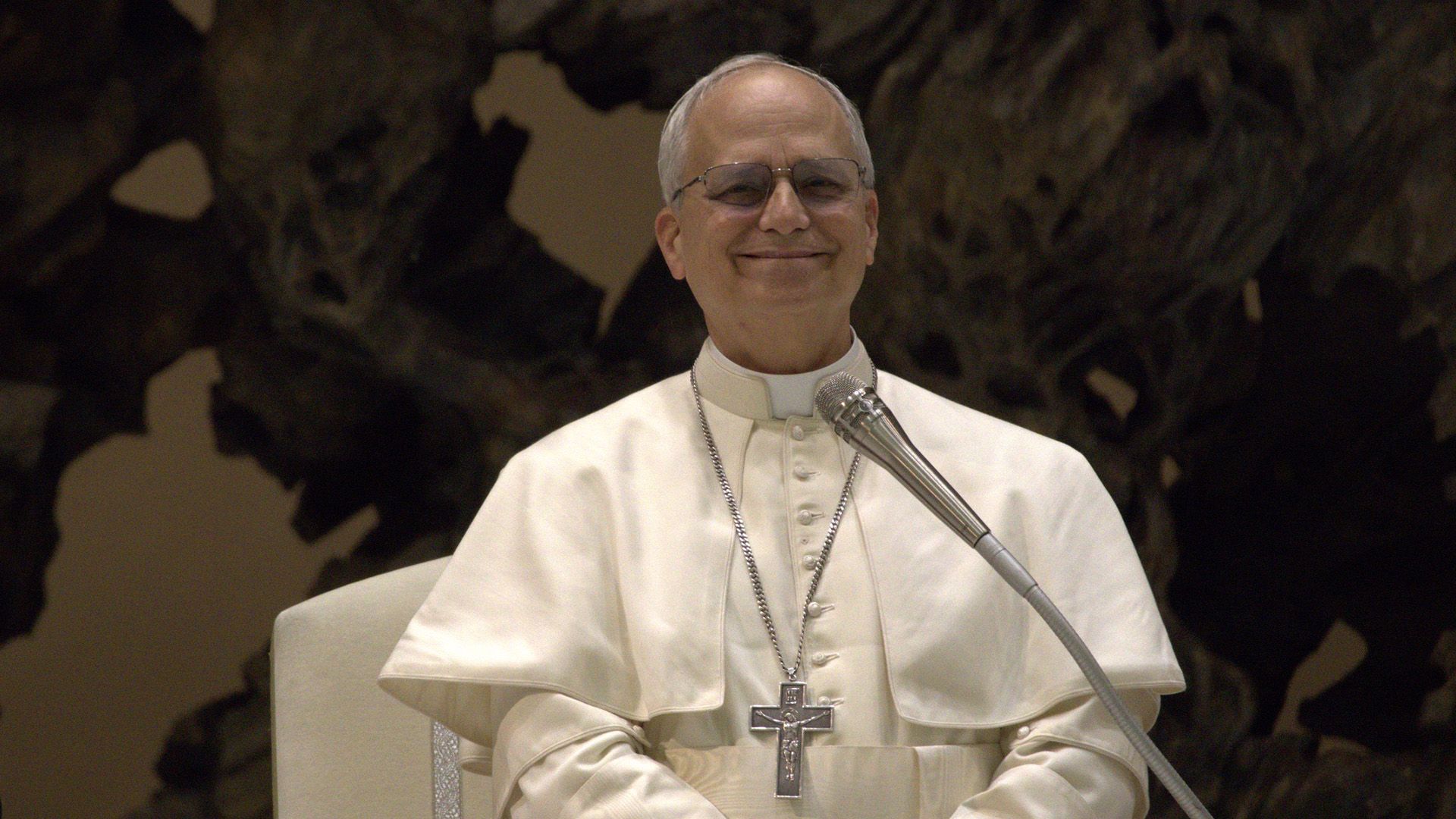Smiling Pope Leo XIV in white clothing on a dark background