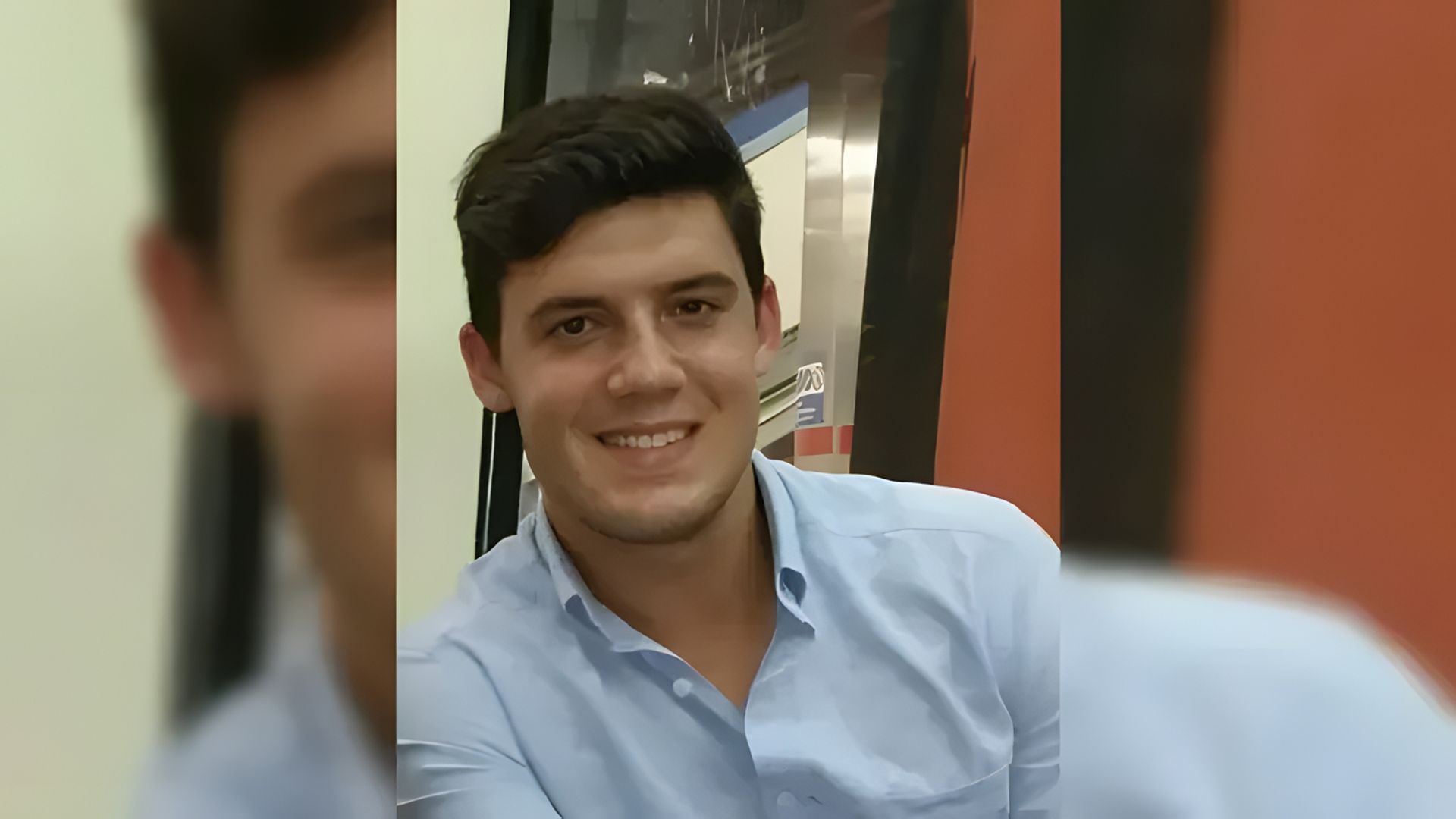 A young man smiles at the camera, the background is blurred