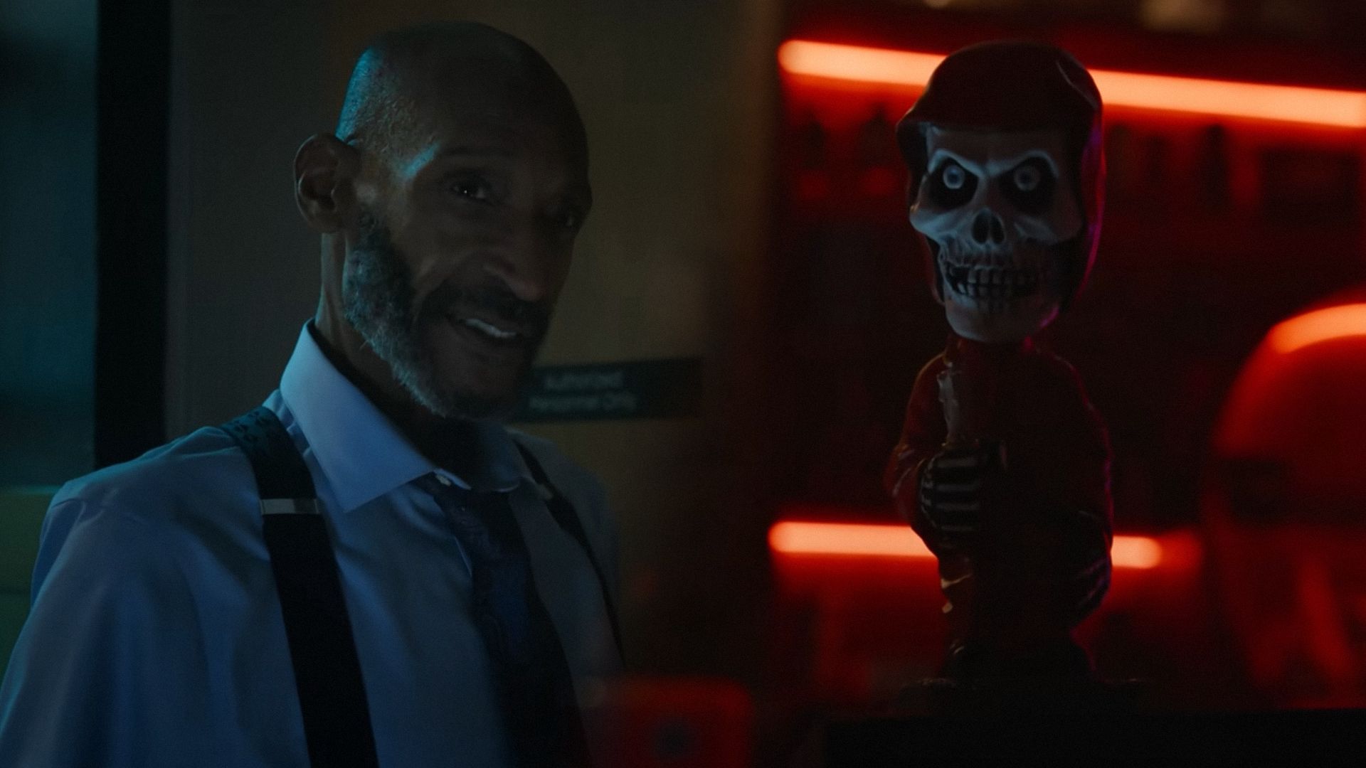 Actor Tony Todd in a white shirt with suspenders stands at an angle and looks sideways against the background of an office