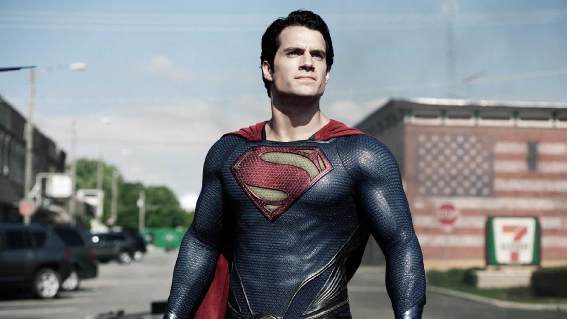 Henry Cavill in a Superman suit looks up while standing on the street