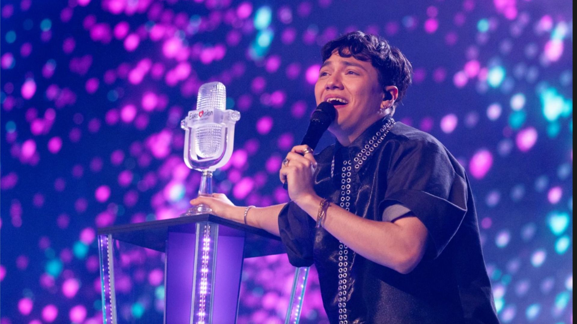 Singer JJ stands on stage by the pedestal with the statuette of the Eurovision 2025 contest and smiles