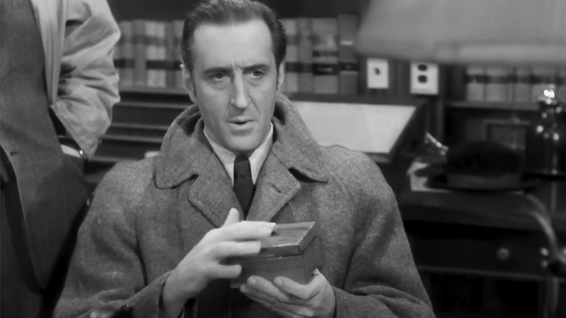 Actor Basil Rathbone as Sherlock Holmes holds a box in his hands and looks down