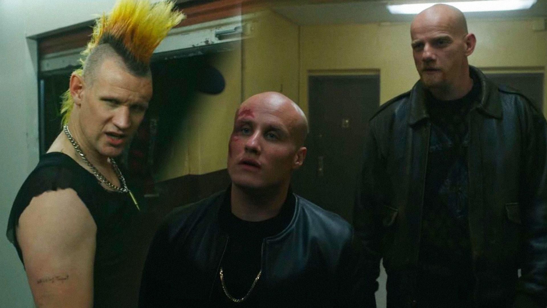 Actor Matt Smith with a mohawk looks to the side, actors Nikita Kukushkin and Yuri Kolokolnikov in leather outfits stand in the hallway and look to the side