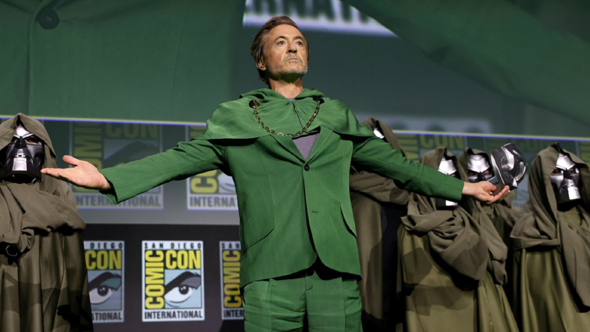 Robert Downey Jr. in a green suit stands on stage, arms outstretched