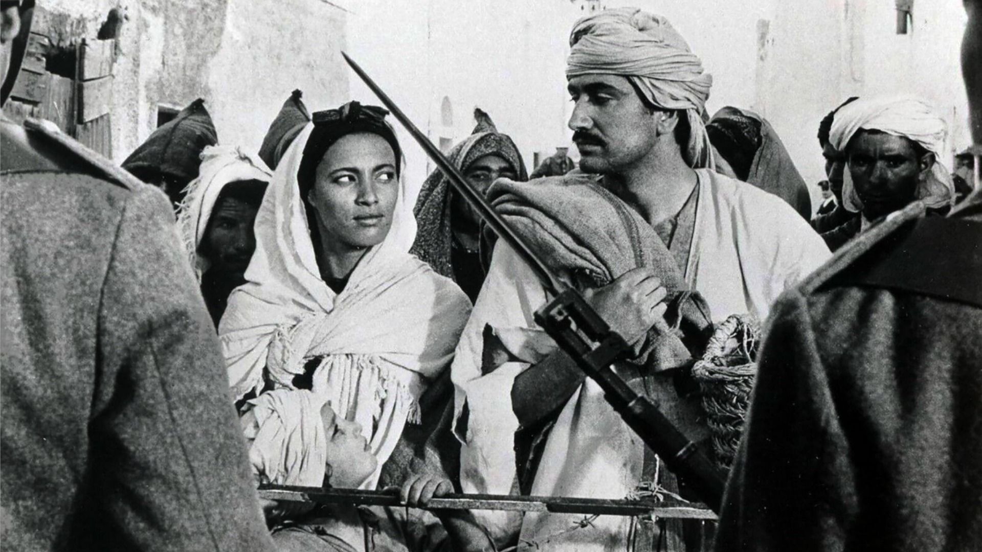 A man and a woman in white clothing look at each other next to soldiers