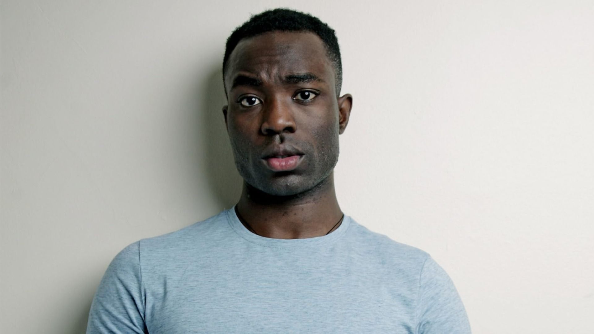Actor Paapa Essiedu stands in blue clothing and looks at the camera, raising an eyebrow