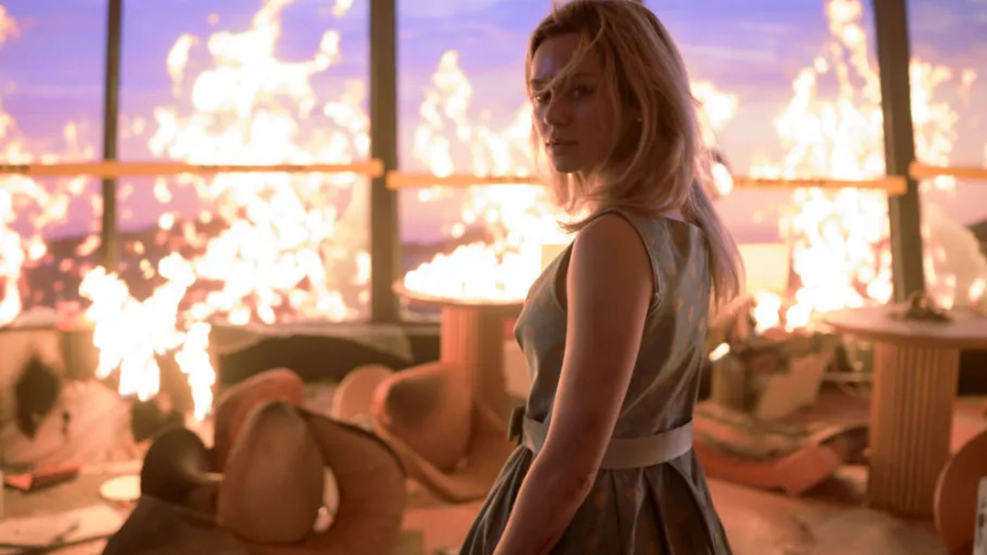 A girl stands against the background of fire