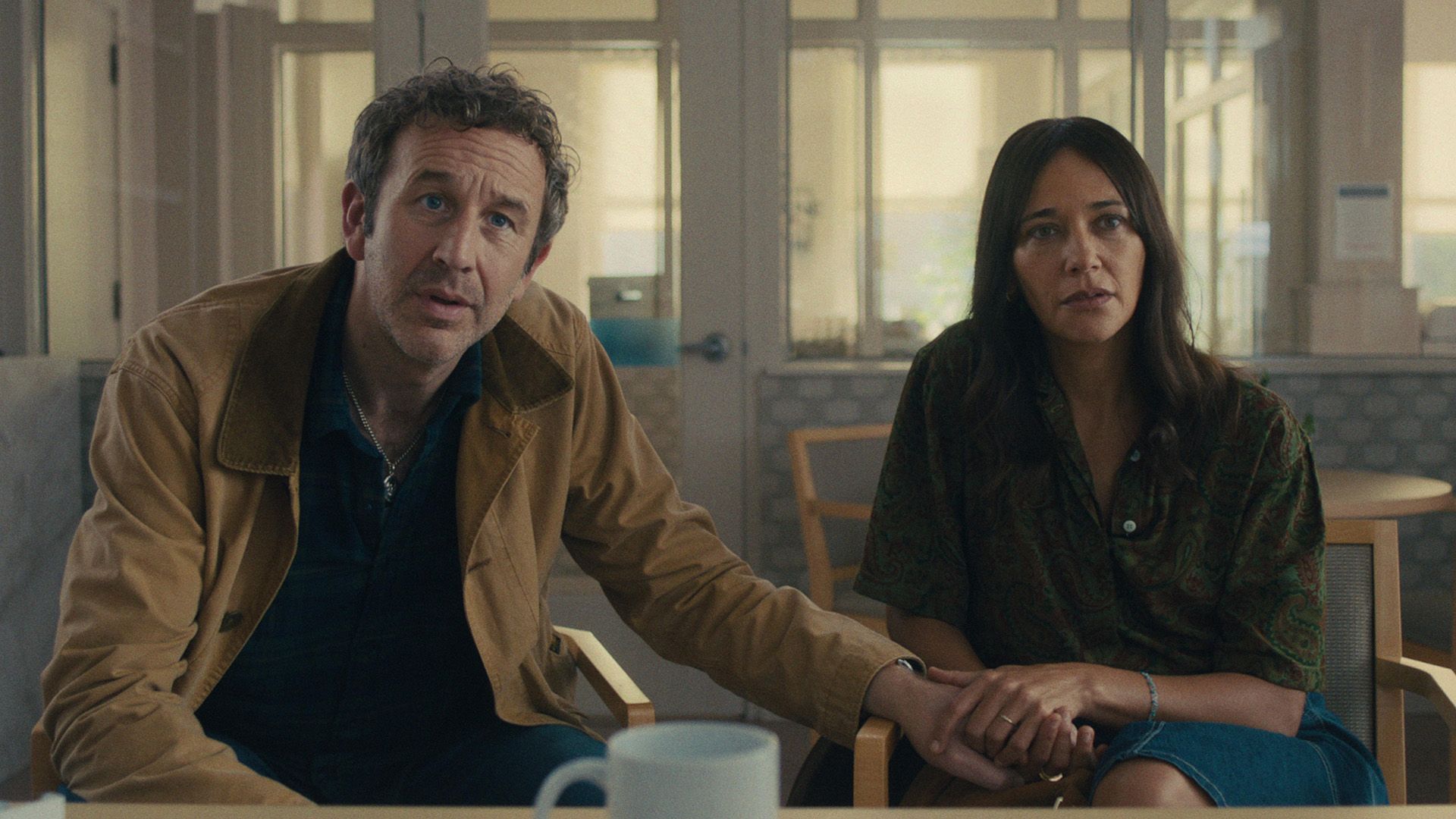Chris O'Dowd and Rashida Jones sitting in chairs with worried expressions, holding hands