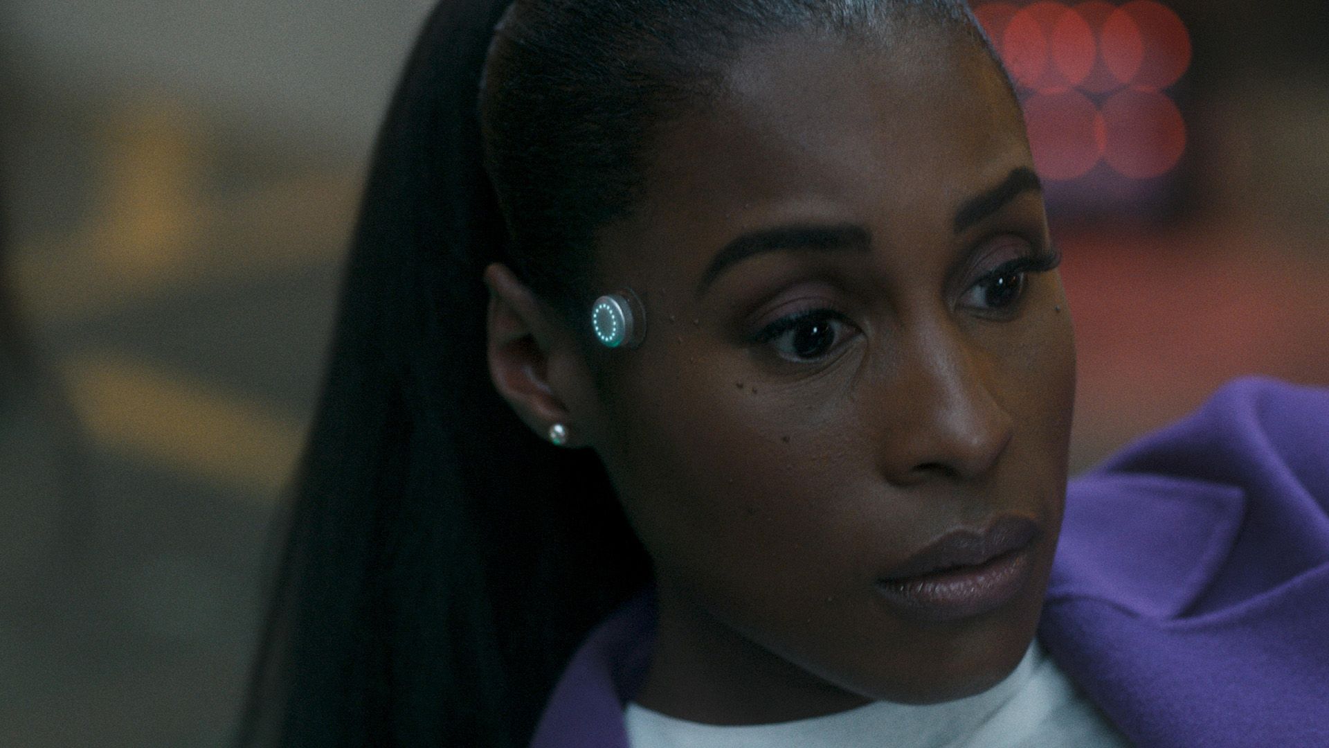 Issa Rae gazes thoughtfully to the side, with a round metallic indicator glowing on her temple