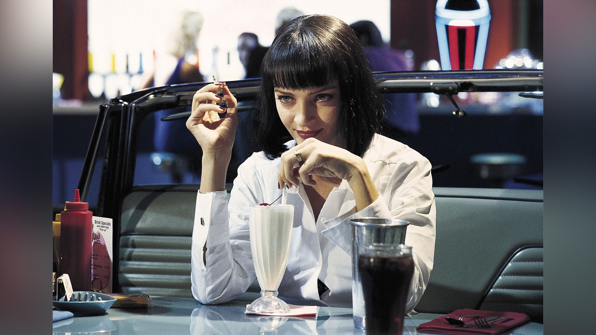 Uma Thurman in a white shirt drinks a milkshake in a café in a scene from the movie 'Pulp Fiction'