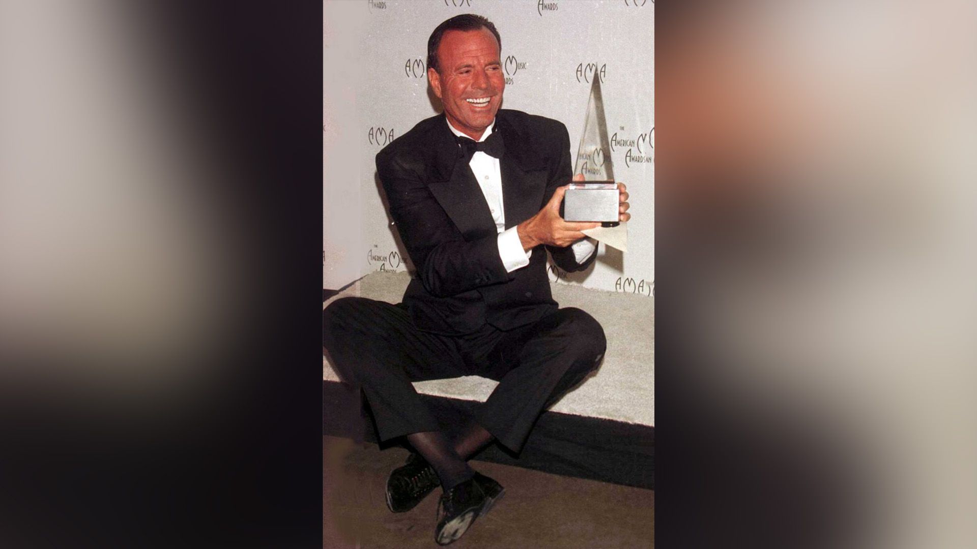 Happy Julio Iglesias in a black suit holds the American Music Awards trophy in his hands