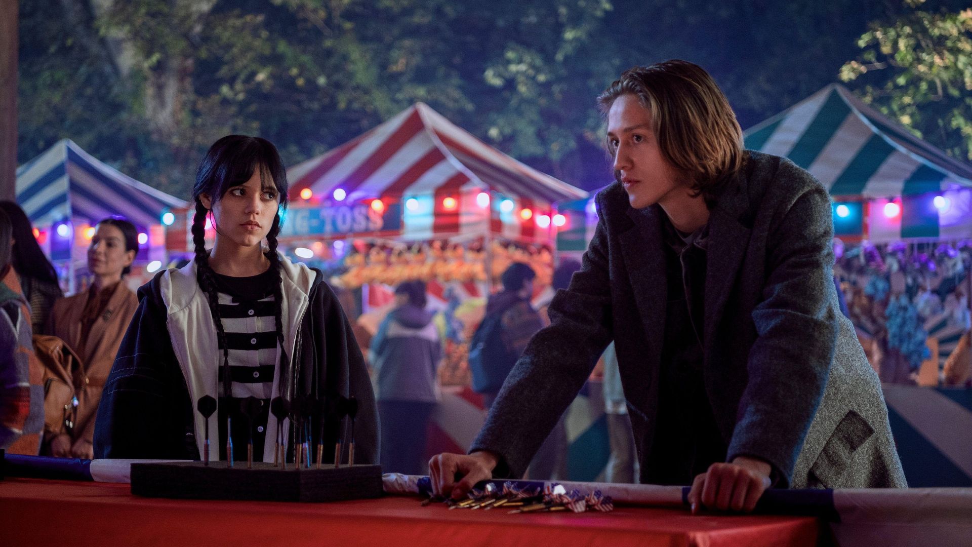 Jenna Ortega and Percy Hynes White in close-up with a fair in the background