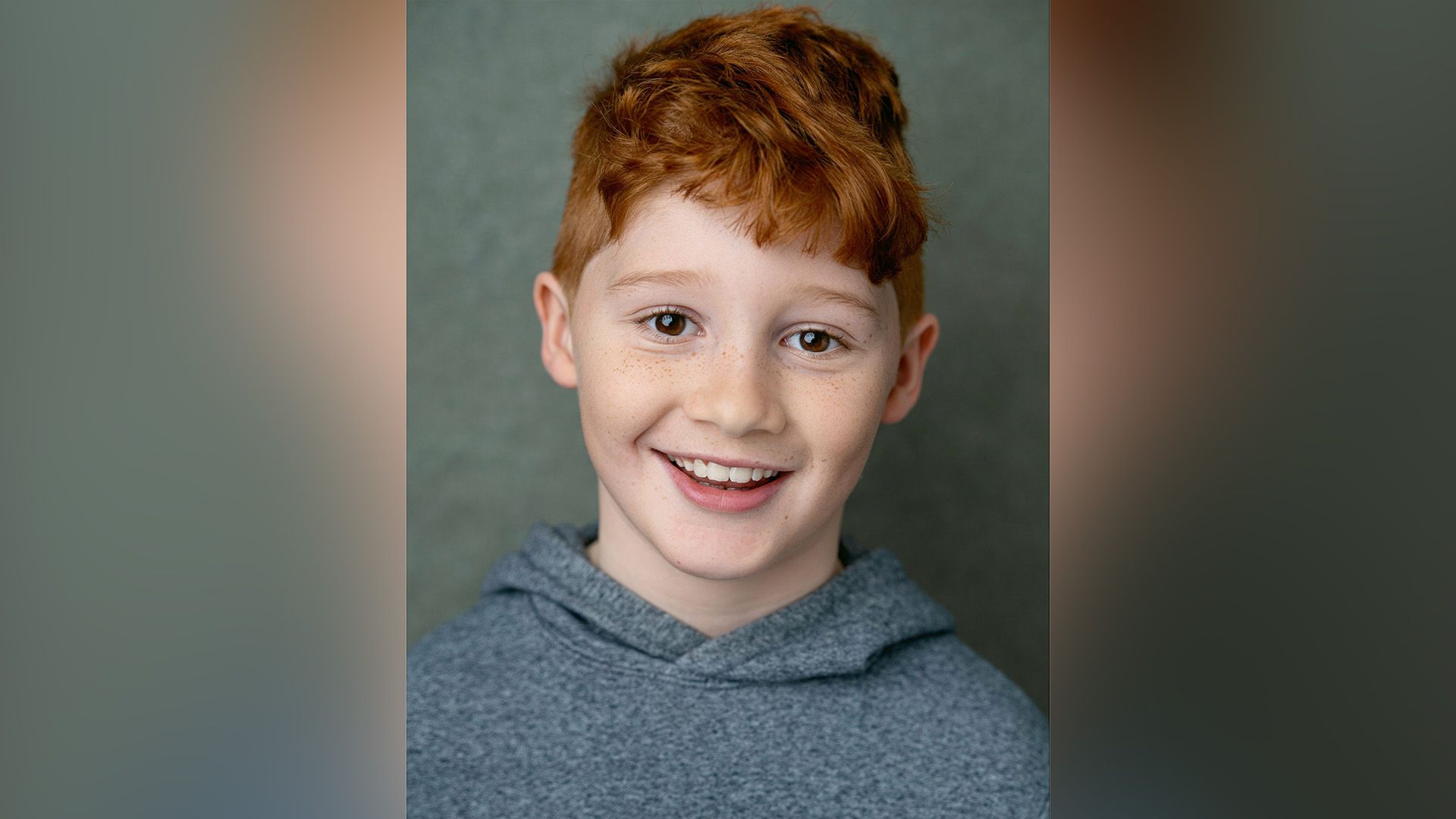 Actor Alastair Stout in a gray hoodie smiling widely