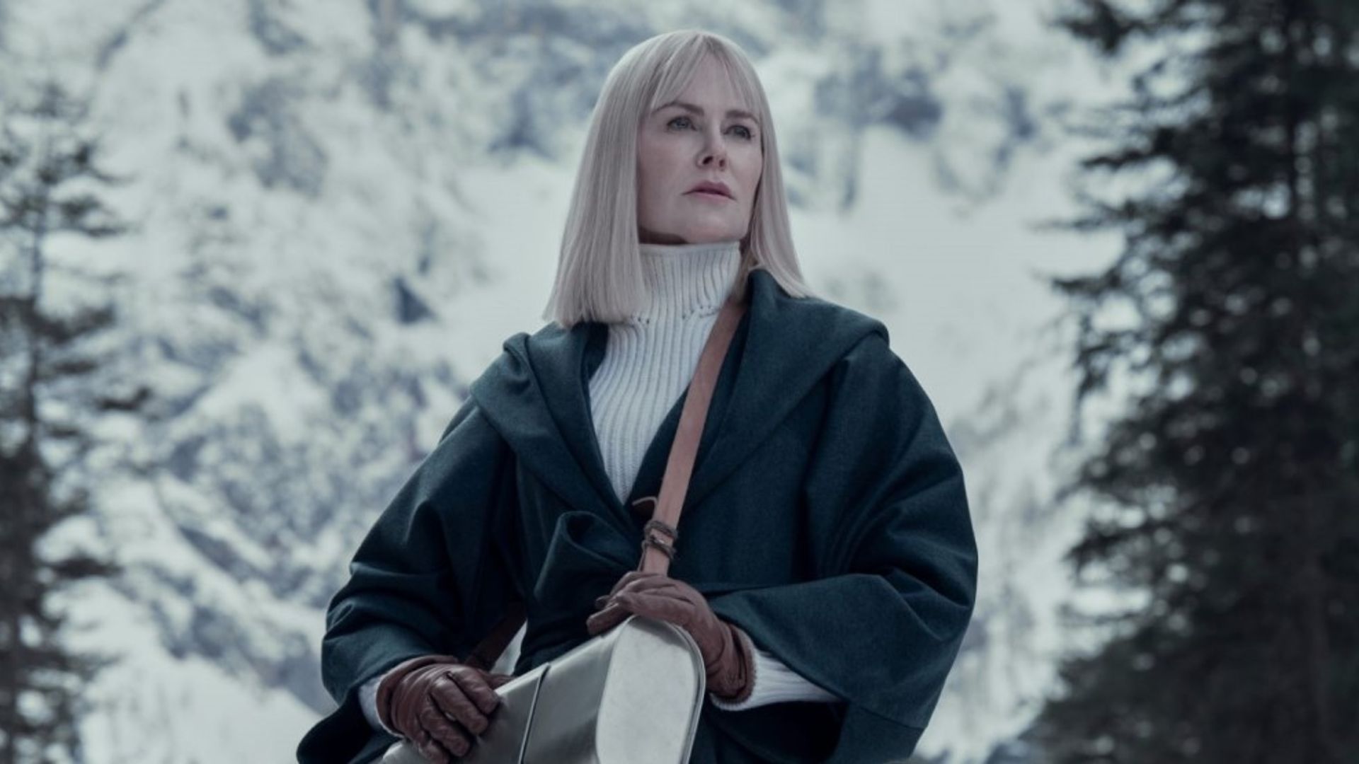Nicole Kidman with straight white hair in a black leather coat and white sweater