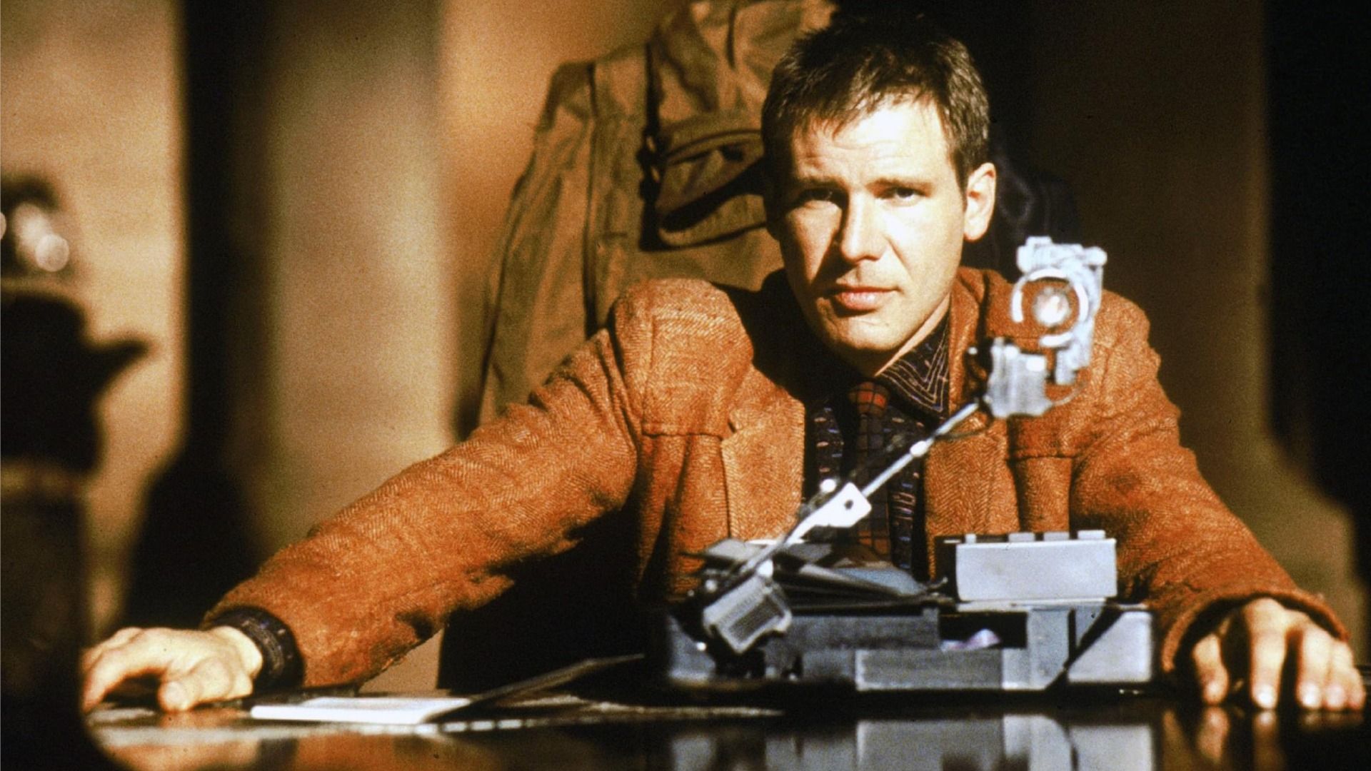 Actor Harrison Ford as Rick Deckard sits at a table in a brown jacket