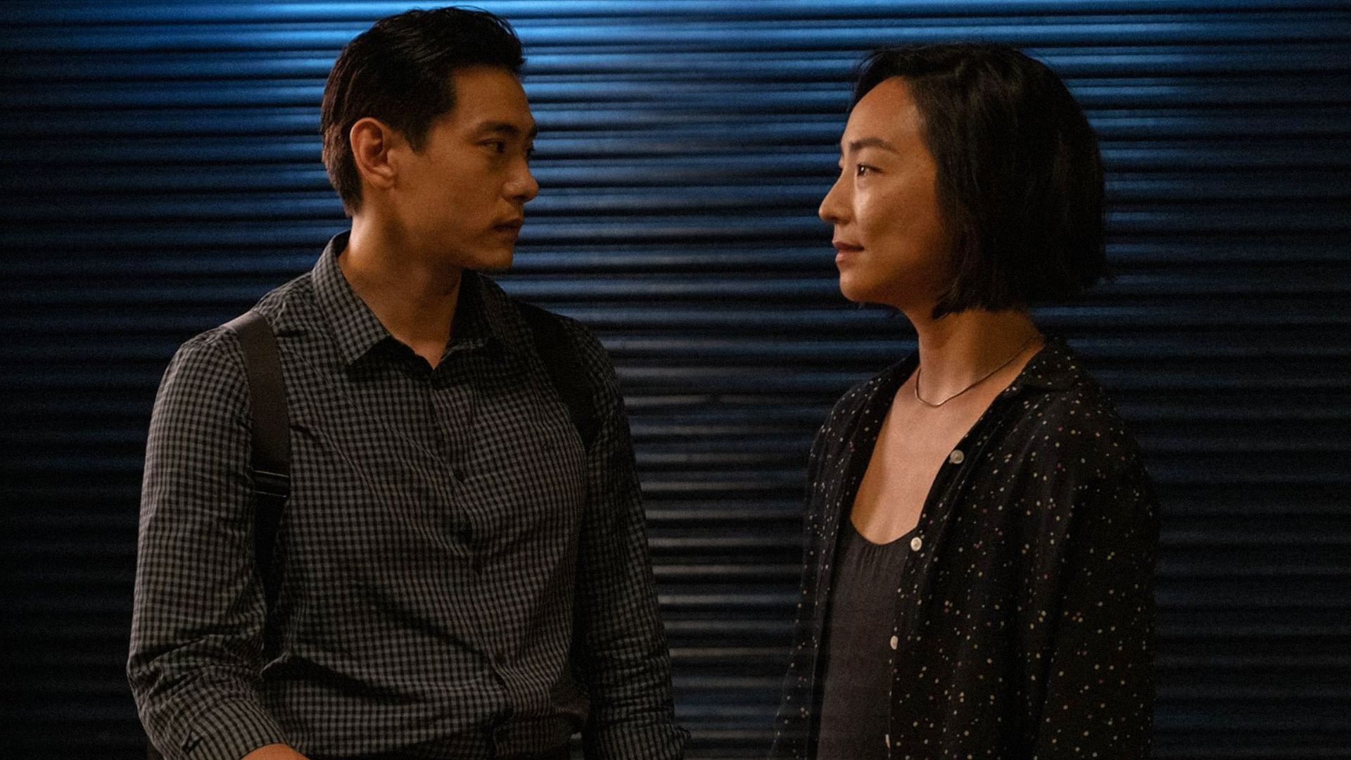 A man and woman look at each other against a wall illuminated with blue light