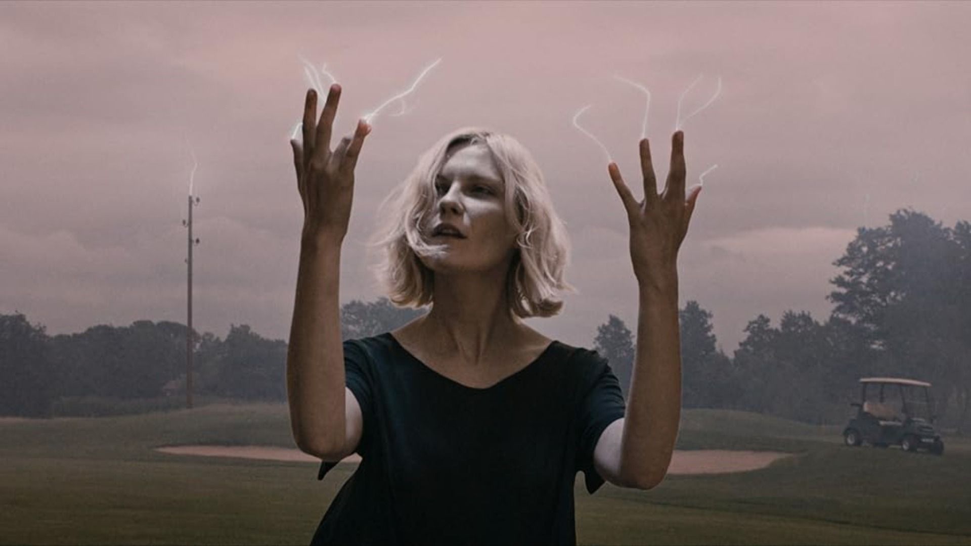 Actress Kirsten Dunst looks at her fingers from which small lightning bolts are emanating