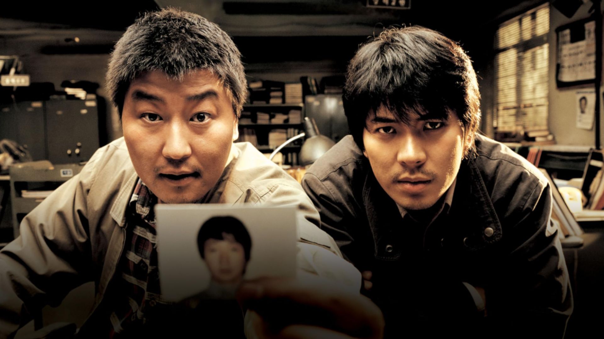 Two men looking at the camera and showing a photograph of a person with black hair