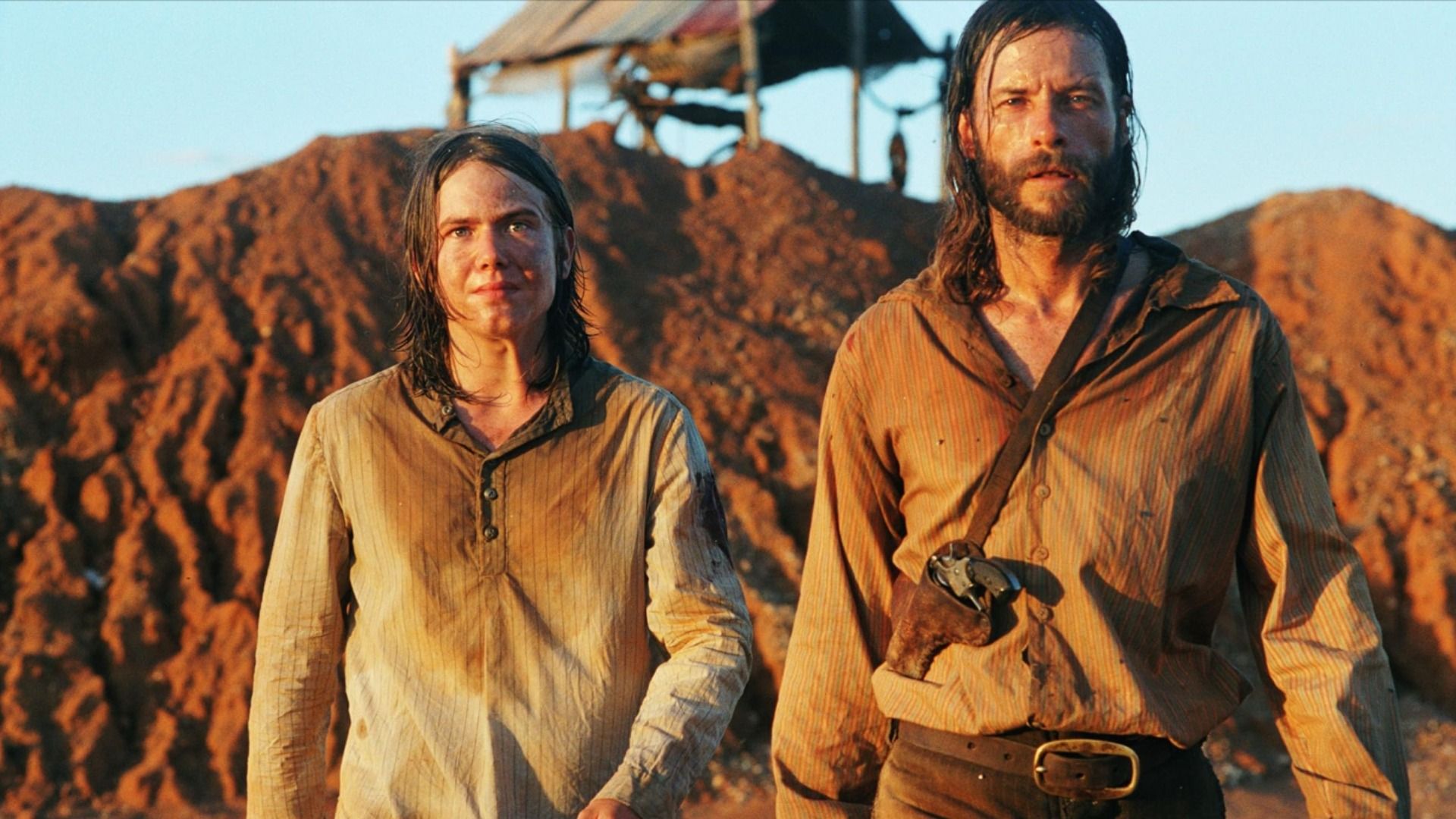 Two men in dirty clothes walking against a sandy background